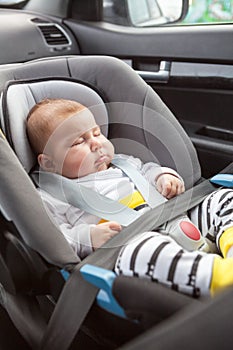 Newborn Caucasian child sleeping in car safety seat, fasten with belts at front passenger chair