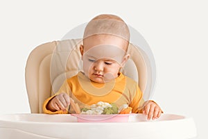 A newborn child aged one year tries boiled vegetables for the first time. A baby carefully takes a boiled carrot while sitting on