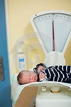 Newborn child after birth in hospital. Adorable cute baby on scale for measuring weight