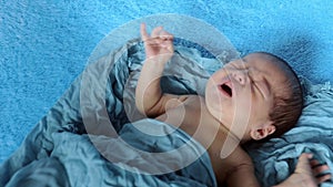 Newborn crying baby boy. New born child tired and hungry in bed under blue knitted blanket. Children cry. Bedding for