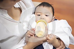 Newborn cute baby is drinking milk from bottle by mom