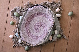 Newborn digital background - oval woven bowl with pink faux fur, jute layer and easter eggs on wooden background. Newborn easter