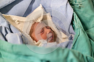 Newborn, eyes closed, crying baby in green blanket in hospital