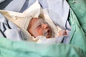 Newborn, eyes closed, crying baby in green blanket in hospital