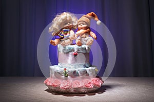 Newborn gift concept. Cake of diapers. Wrapped diapers as cake with flowers. Cake of wrapped clean diaper on table with baby doll