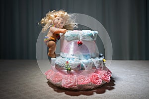 Newborn gift concept. Cake of diapers. Wrapped diapers as cake with flowers. Cake of wrapped clean diaper on table with baby doll