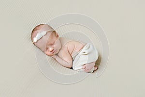 Newborn girl in hairband sleeping on her side