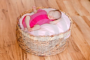 Newborn girl in pink bodysuit barefoot lies in round crib and sleeps