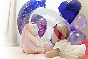 A newborn girl in a red skirt and a red bow on her head is lying on the bed next to a plush toy rabbit. Baloons, Infante