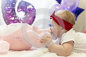 A newborn girl in a red skirt and a red bow on her head is lying on the bed next to a plush toy rabbit. Baloons, Infante