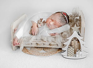 Newborn Girl Sleeping On Small Bed With Toy Deer And Tiny Christmas Tree Nearby