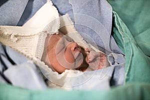 Newborn in the green blanket in the hospital, baby with eyes closed