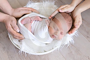 A newborn in the hands of parents, a baby sleeping in his father`s and mother`s hands on a white background, a happy family