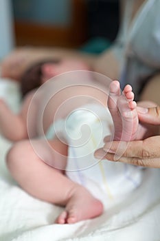Newborn infant barefoot leg in women hand, mother breastfeeding baby lying in bed, close up view