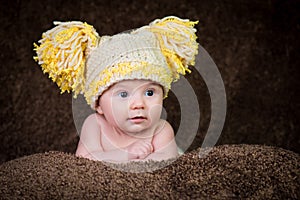 Newborn in knitted winter hat on a beige background.