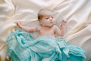 Newborn lies on a beige blanket covered with a blue scarf