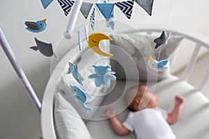 Newborn lies in the round white bed with mobile