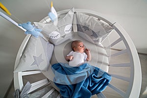 Newborn lies in the round white bed with mobile