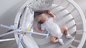 Newborn lies in the round white bed with mobile