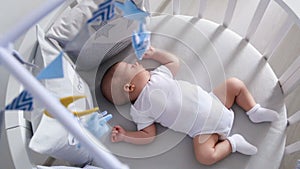 Newborn lies in the round white bed with mobile