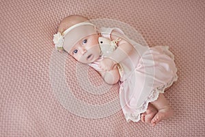 Newborn little girl in a soft pink dress on a pink powdery blanket, background