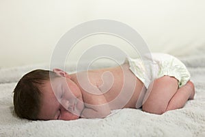 Newborn male caucasian baby sleeping on white blanket with diaper