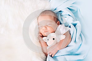 Newborn sleep at first days of life. Portrait of new born baby one week old with cute soft toy in crib in cloth background