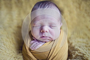Newborn sleeping baby boy or girl picture like newborn potato in yellow wrap on furry blanket background