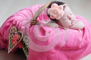 Newborn sleeping. Infant baby girl closeup lying on pink blanket in basket decorated with wooden heart