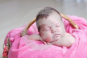 Newborn sleeping. Infant baby girl lying on pink blanket in basket. Cute portrait child.
