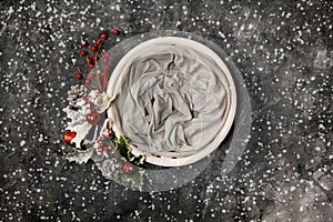 Newborn winter background - round cream bowl with CHristmas red berries and snow covered branches  garland on dark backdrop