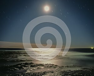 Star trails over pacific ocean bright moon shining on water landscape colour night Newcastle New South Wales Australia
