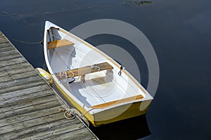 Newer yellow and white rowboat sits moored on a calm quiet harbr