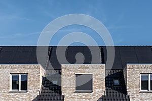 Newly build houses with solar panels attached on the roof against a sunny sky Close up of new building with black solar