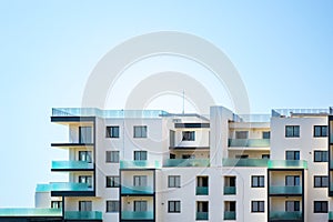 Newly built apartments building on a bright blue sky, with space for text on top. Upper part of a white building.