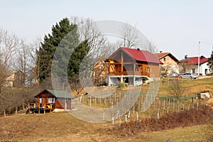 Newly built modern wooden log house with big open porch in front on side of small hill above small wooden storage shed