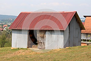 Newly built outdoor barn covered with large red and grey metal sheets for protection filled with hay bales on side of small hill