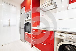 Newly installed bright red open plan kitchen in a room with light laminate flooring and a column of appliances next to a stainless