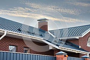 Newly installed construction frame house rain gutter system on the metal roof top. Brick chimney pipe. Automatic metal gates.