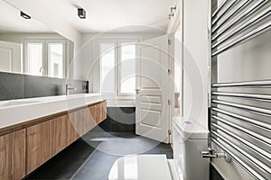 Newly installed designer bathroom with tall wooden cabinet with elongated drawers, two white porcelain one-piece