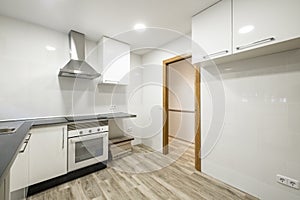 Newly installed kitchen with black stone countertops, gloss white cabinets, wood flooring and stainless steel appliances