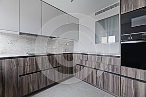 Newly installed kitchen in contemporary design with root wood cabinets, glossy black appliances and gray tile floors