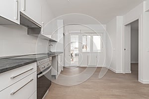 Newly installed kitchen furniture with white wall and base units, gray countertop in an open room with access to a terrace