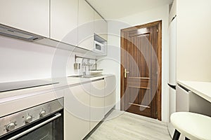 Newly installed kitchen with smooth white cabinets without handles, white stone conglomerate worktop and light laminated flooring