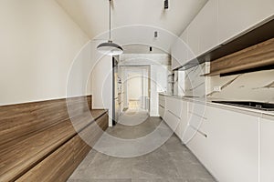 Newly installed narrow walk-through kitchen with white furniture without handles on one side and a long wooden bench with cabinets