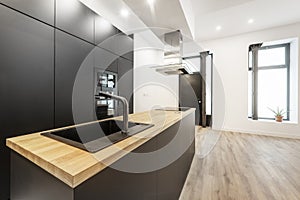 Newly installed open plan kitchen with black cabinets, appliances and faucets and an island with a wood countertop on laminate