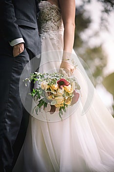 Newly married couple in embrace with the bridge holding a pretty bouquet in a vertical shot