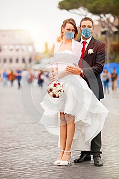 Newly married couple with face mask on their wedding day. On the street with the Colosseum in the background in Rome, Italy. The