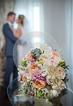 Newly-married couple kissing and wedding bouquet in the foreground.