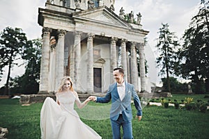 Newly married couple running and jumping in park while holding hands